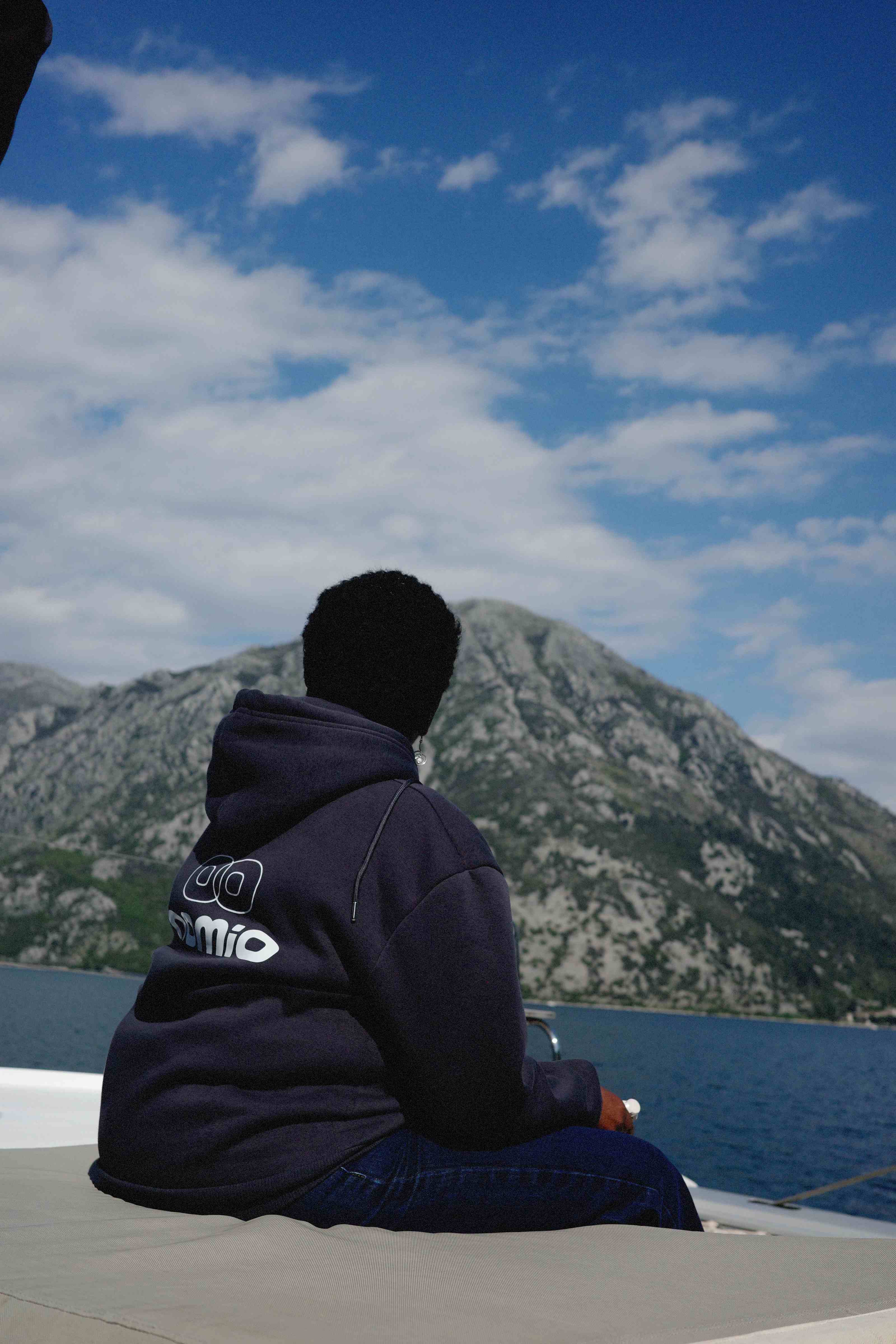 Guest in a Nomio branded hoodie on a boat facing the Kotor mountains
