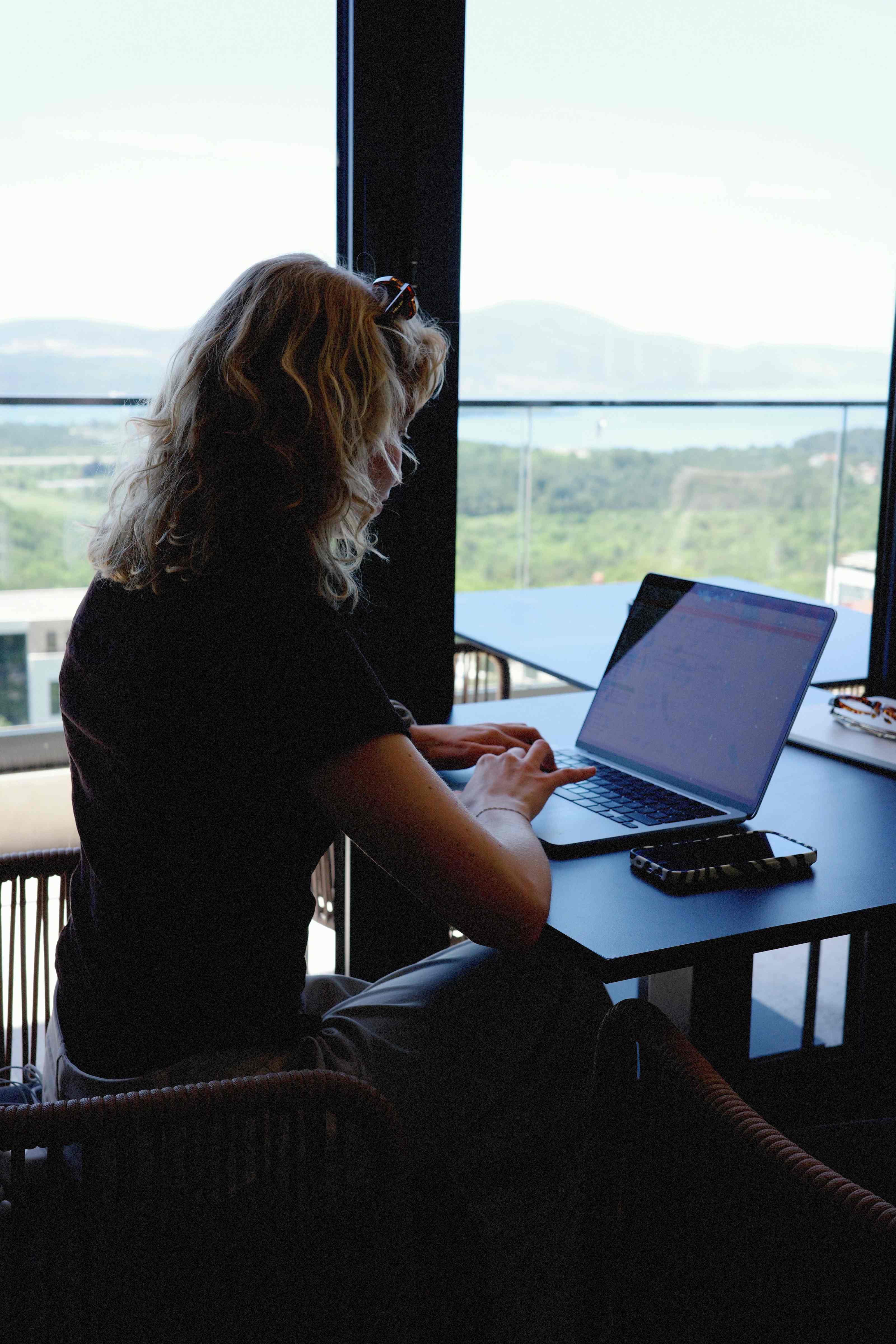 Digital nomad working on a laptop by panoramic windows over the bay