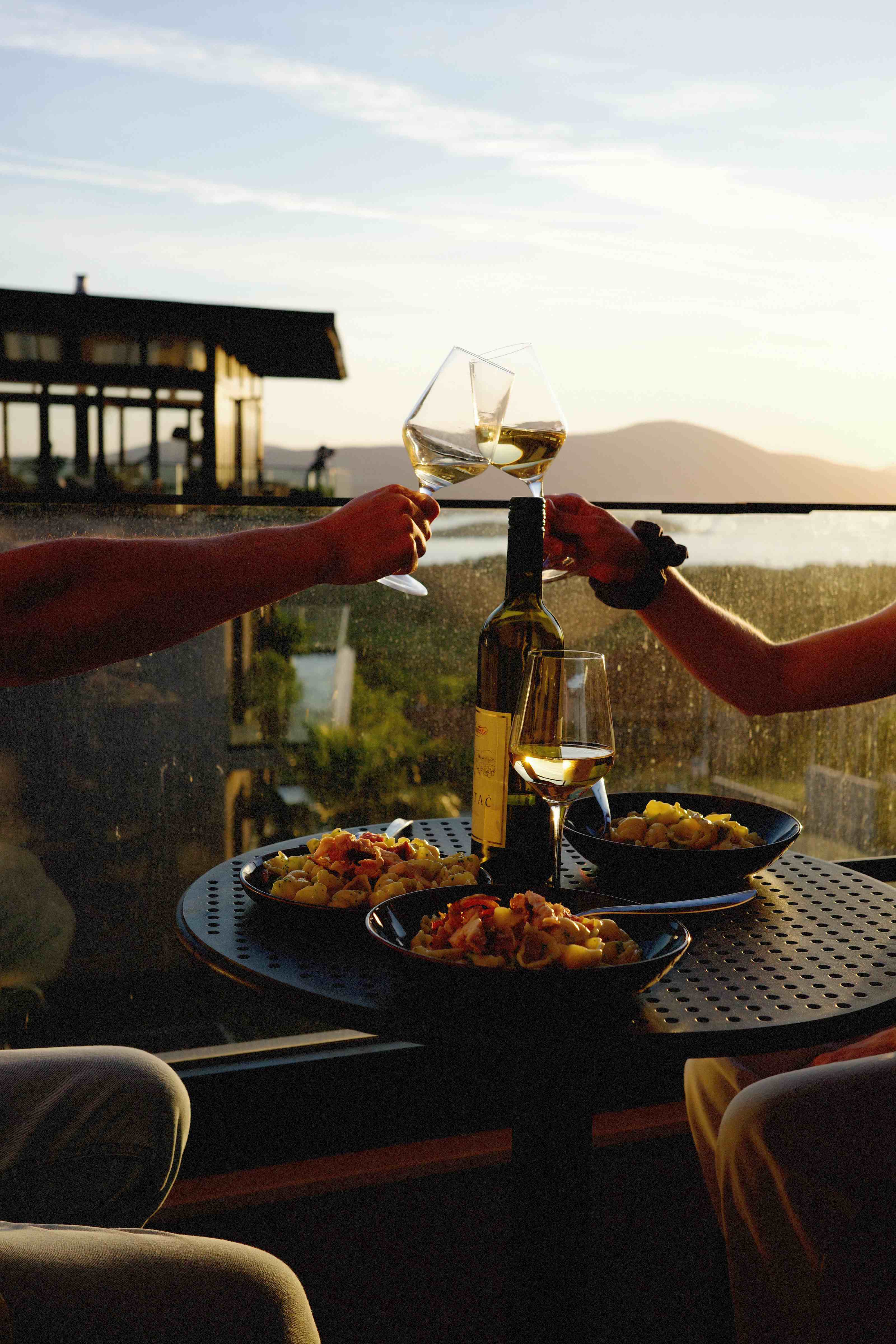Two guests toasting white wine at golden hour with a bay view